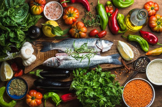 Persona escribiendo un plan de comidas en una libreta con ingredientes frescos al lado.